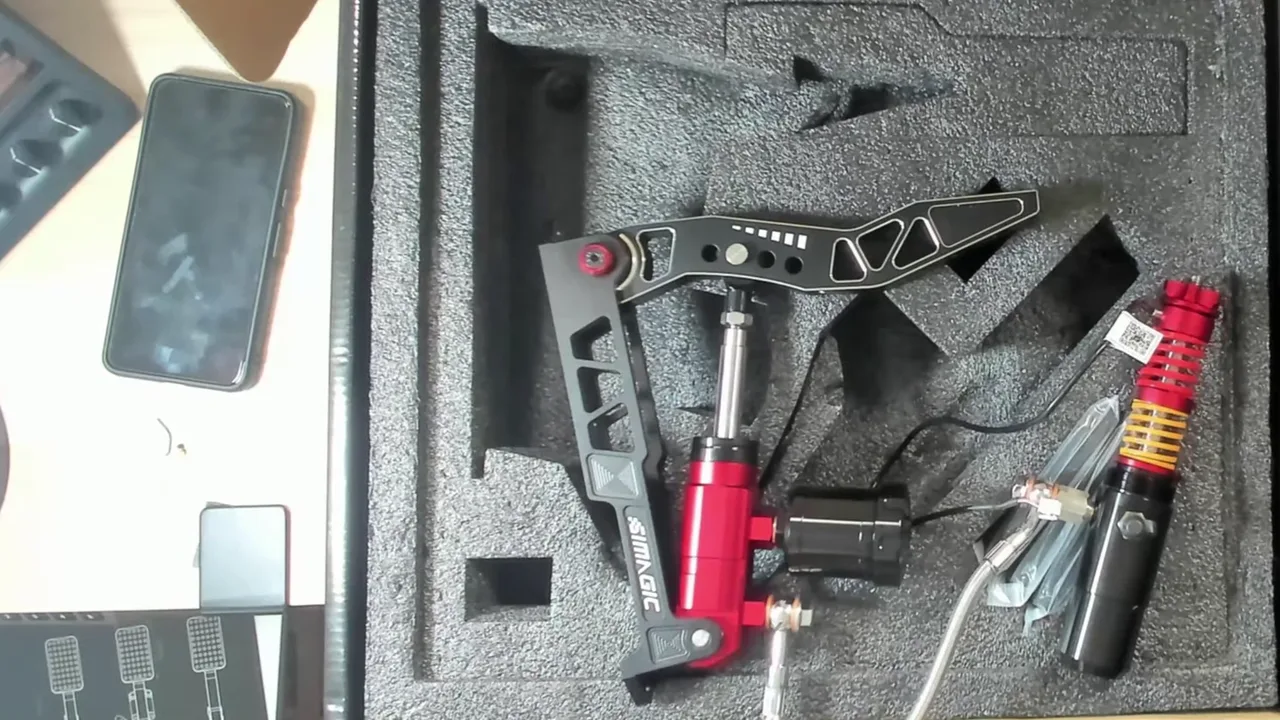 Toute la chaîne du frein d'un coup d'œil : le maître-cylindre rouge sous la pédale, la durite tressée, et le récepteur avec ses ressorts et le câble du load cell.