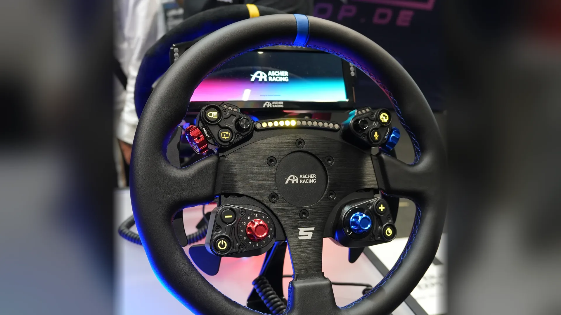 Un autre volant rond Ascher Racing, sur une table du stand : les modules des AURA GT, mais une autre jante, et aucun nom écrit dessus.