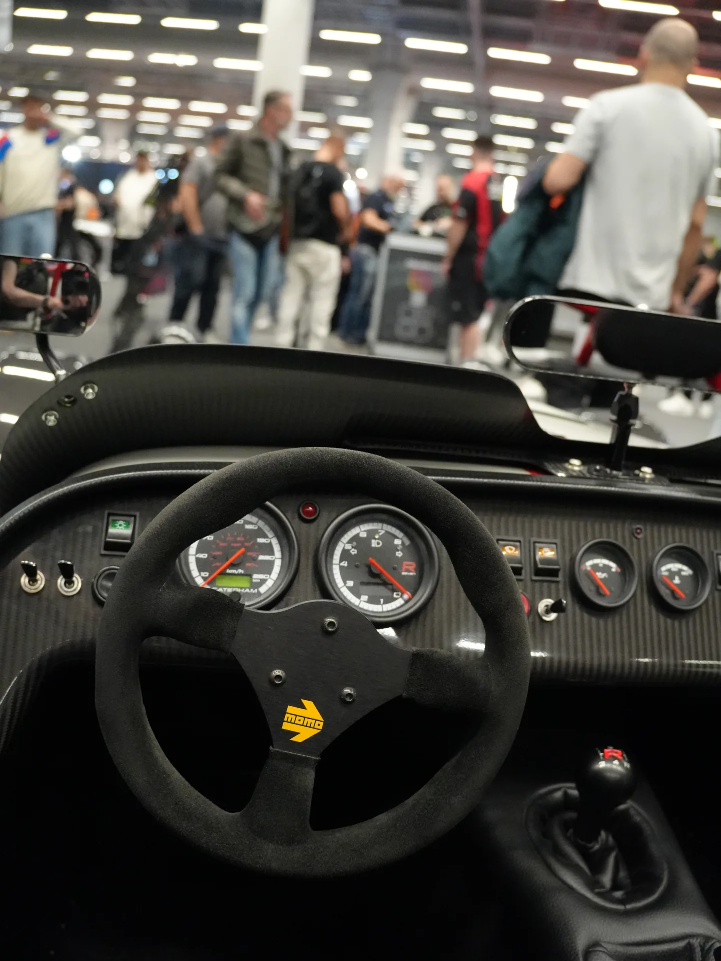 Au volant de la Caterham Seven exposée près du stand BDH, avec le hall 12 derrière. Énormément de stands, énormément de monde aussi.